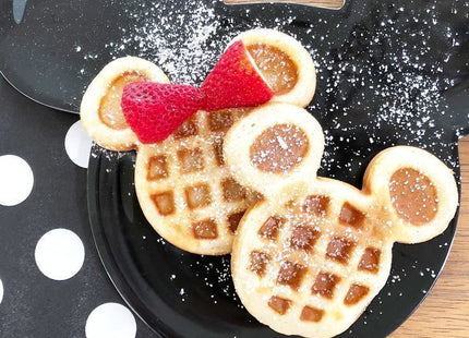 Δύο βαφλάκια σε σχήμα Mickey σε μαύρο πιάτο με φράουλες και ζάχαρη άχνη.